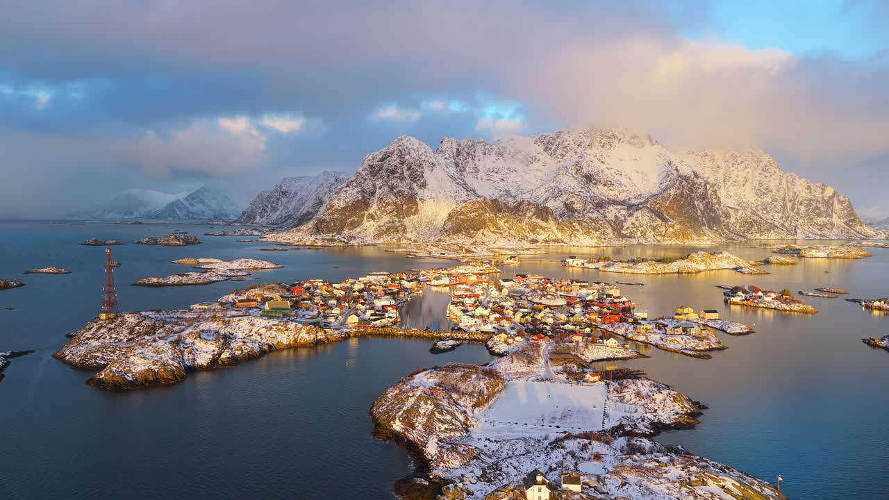 Elokuvamainen ilmakuva ikonisesta Henningsværin kalastajakylästä lumihuippuisten vuorten ja arktisen meren ympäröimänä kultaisen tunnin aikana Lofooteilla, Norjassa.