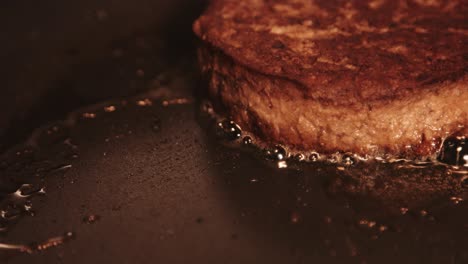 single vegan plantbased burger cooking and sizzling in hot pan with oil bubbling