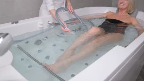 a young woman lies on her back in a bathtub during a hydromassage. professional water procedures. peeling procedure for weight loss and rejuvenation. vertical video