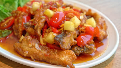 pescado de mero frito cubierto con salsa dulce, agria y picante en un plato blanco - estilo de comida asiática