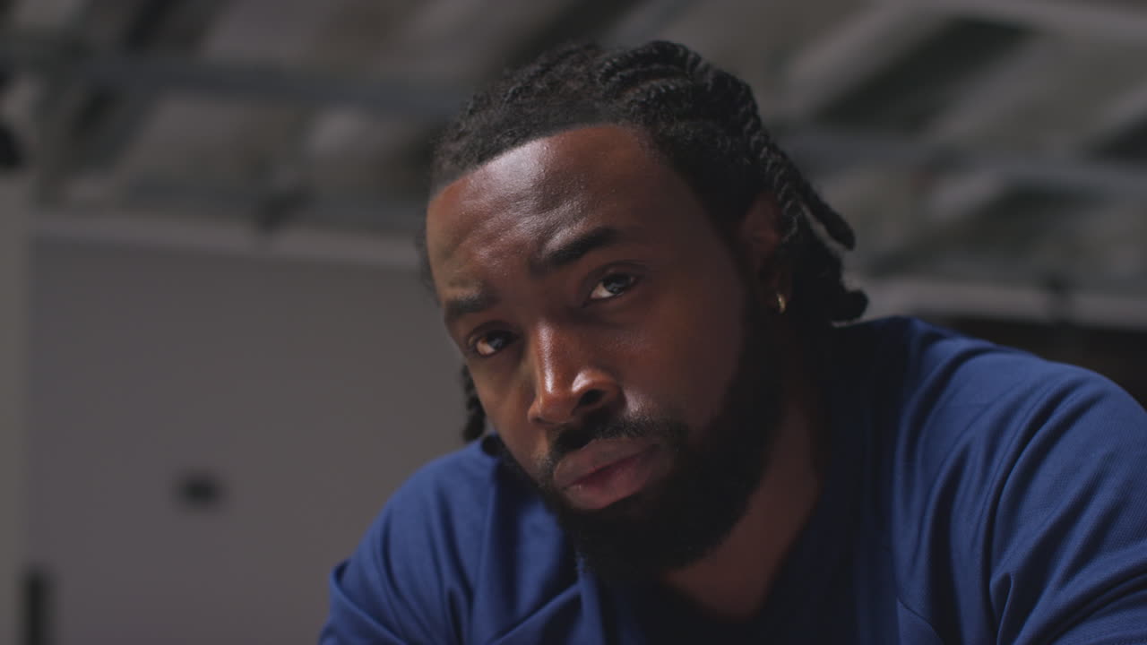 retrato en primer plano de un atleta masculino decidido entrenando en el gimnasio sentado y concentrado en el vestuario con una expresión enfocada 1