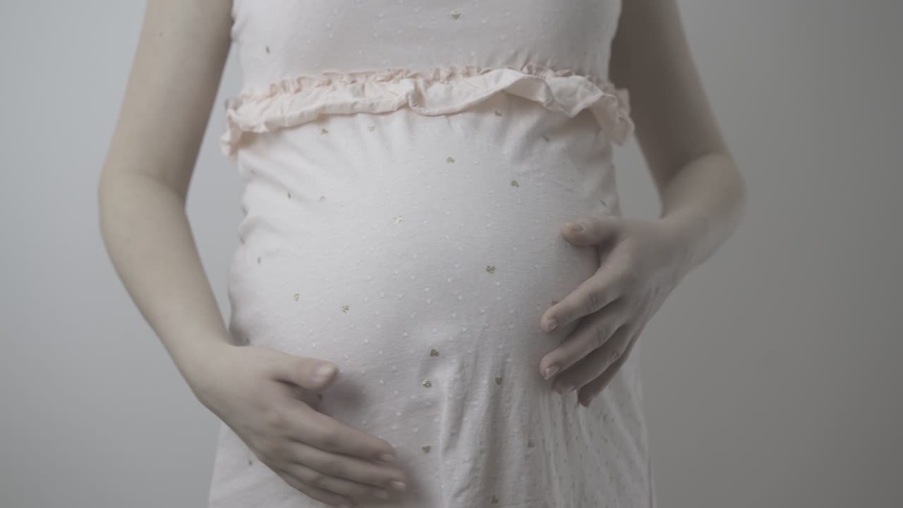 la futura madre en vestido rosa acaricia el estómago en un primer plano de la pared