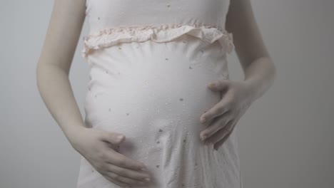 future-mother-in-pink-dress-strokes-tummy-at-wall-closeup