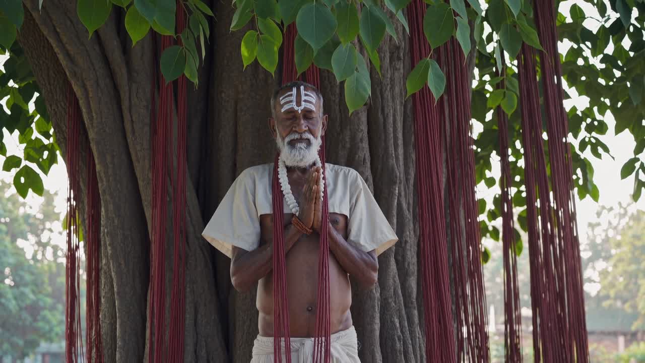 White beaded sadhu meditating, forehead marked with sacred markings, sitting beneath tree adorned with crimson ritual threads in traditional spiritual setting