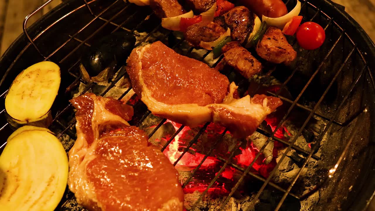 Close-up view of steaks and vegetables sizzling on a charcoal grill, showcasing vibrant colors and textures.