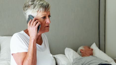 sick senior man lying on bed while woman talking on mobile phone