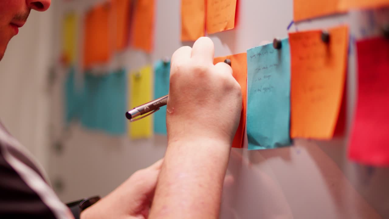el hombre enfocado escribe en una nota pegajosa, planeando y haciendo lluvia de ideas en el entorno de la oficina.