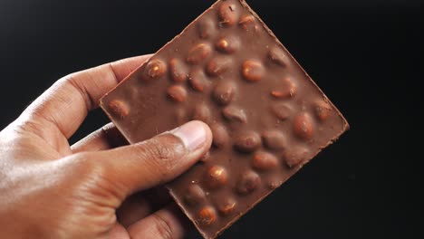 hand holding a square of dark chocolate with hazelnuts