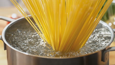 los espaguetis colocados verticalmente en la olla de agua hirviendo se extienden en todas direcciones, tocando el borde de los utensilios de cocina