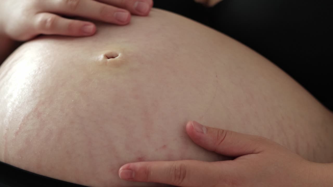 Close up of pregnant woman lying down, rubbing her belly. Third trimester