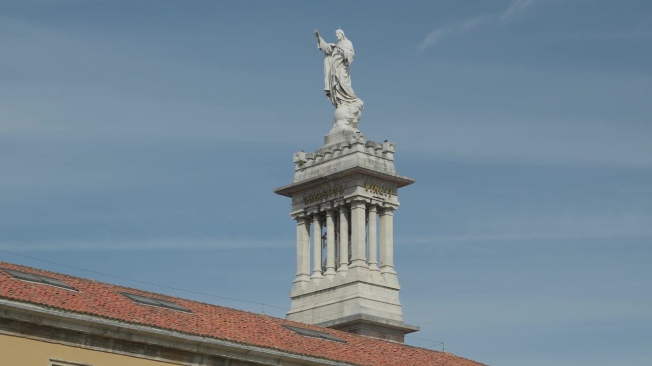 Primo piano medio della statua in marmo bianco di Gesù Cristo in cima alla storica torre della Basilica del Sacro Cuore sopra un tetto di tegole a Gijon, Asturie, Spagna.