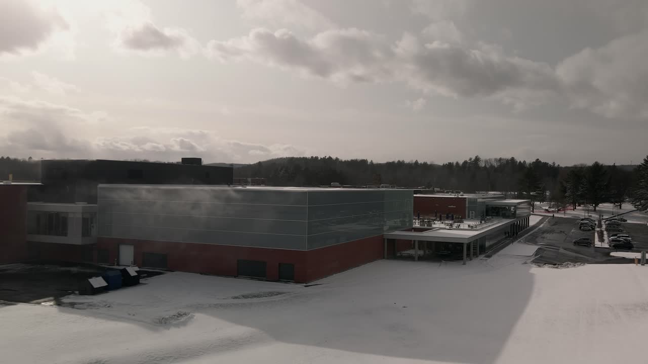 drone volando lejos del edificio del centro deportivo de la universidad del obispo cerca del campo coulter durante el invierno en sherbrooke, quebec, canadá