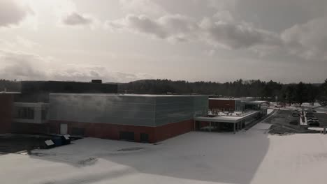 drone flying away from building of bishop's university sports center near coulter field during winter in sherbrooke, quebec, canada