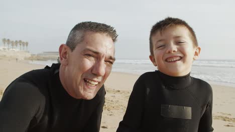 father and son in wetsuits smiling at camera