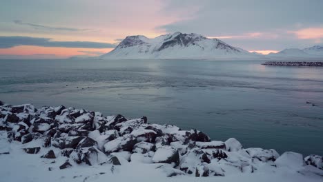 snowy banks are seen on the snaefellsne peninsula in iceland at sunset with birds swimming in the water