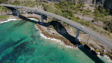 bird's eye view of sea cliff bridge with several vehicles driving across grand pacific drive near wollongong, nsw australia