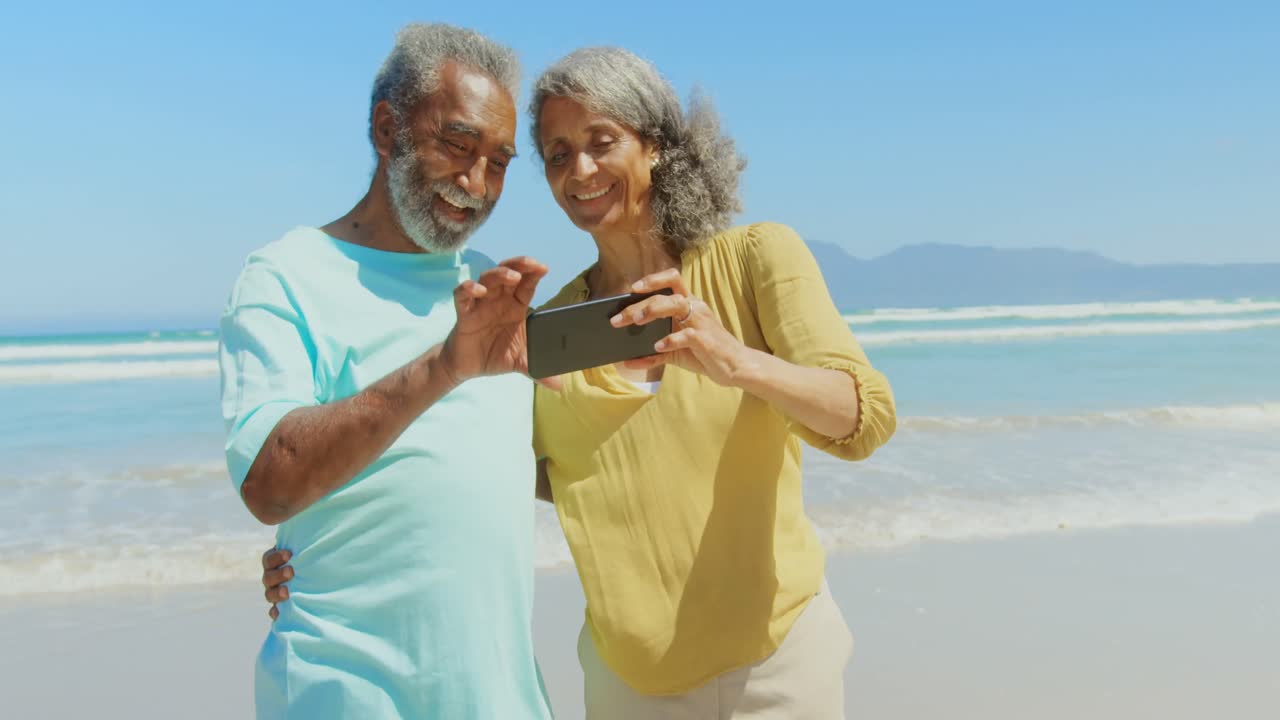 Front view of active senior African American couple taking selfie with mobile phone on the beach 4k