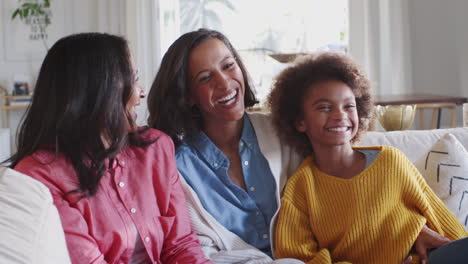 Grupo-Familiar-Femenino-De-Tres-Generaciones-Sentado-En-Un-Sofá-Viendo-La-Televisión-Riendo-Juntos,-De-Cerca