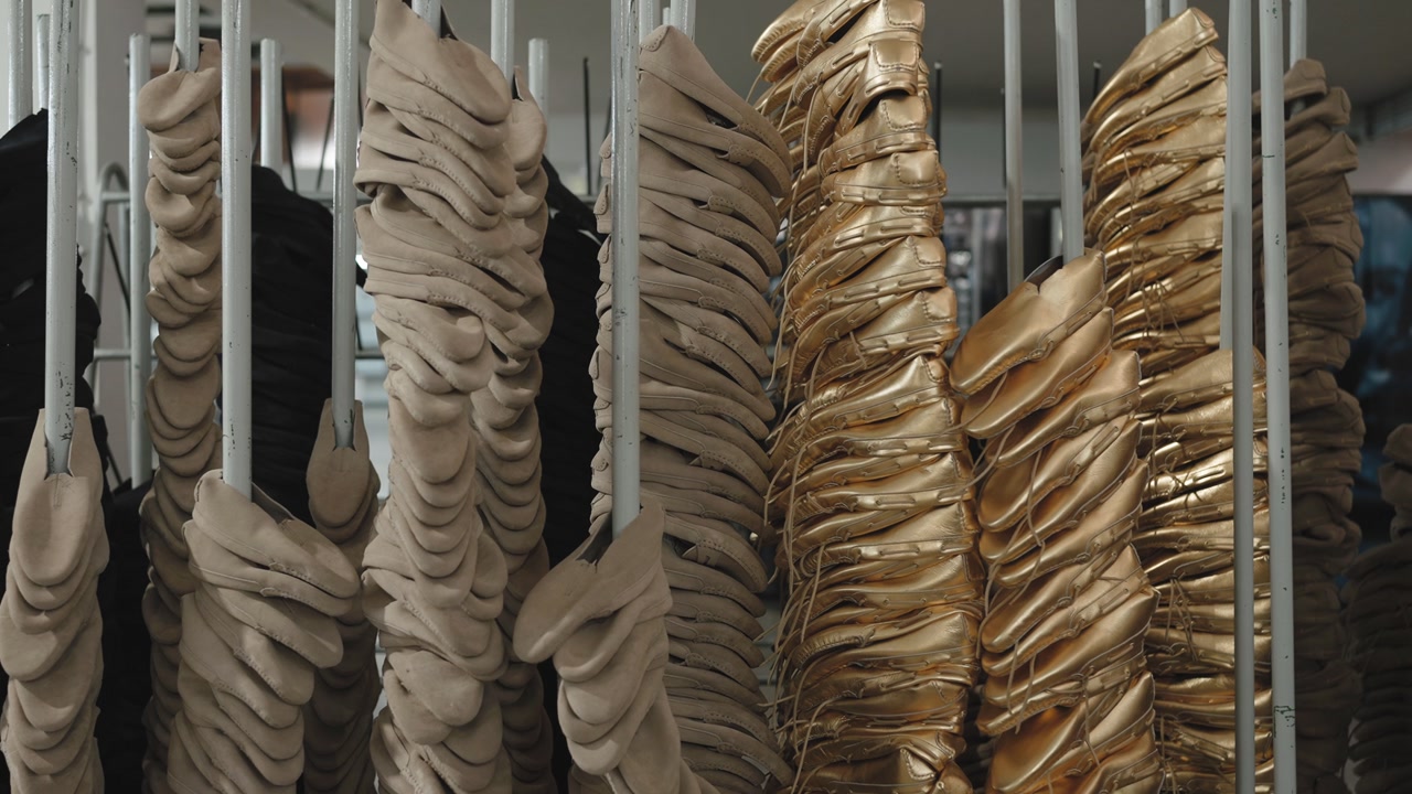 Rows of beige and gold satin ballet pointe shoes stacked and hanging on white metal poles in a dance shoe manufacturing factory