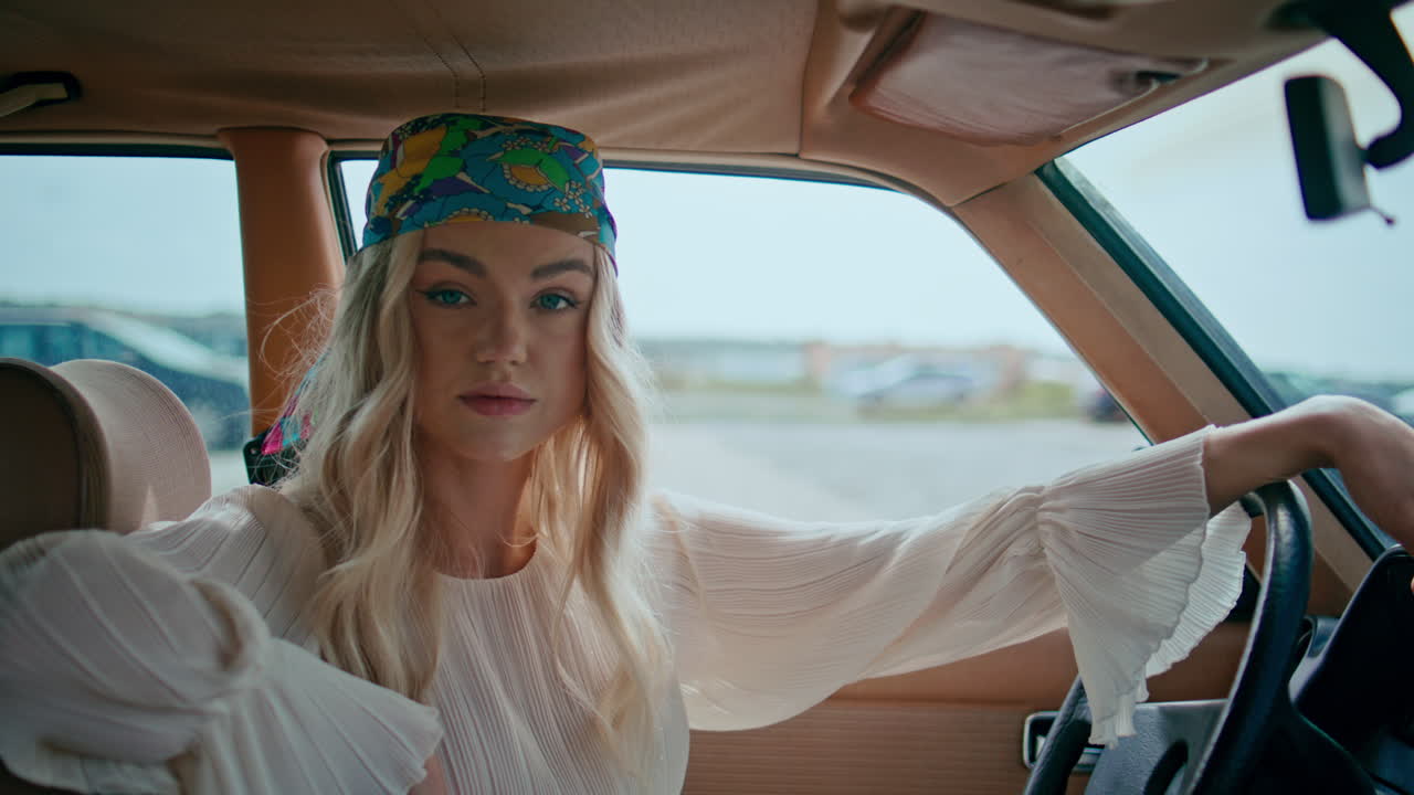 chica sentada en el salón de automóviles poniendo la mano en el volante usando un pañuelo de cerca