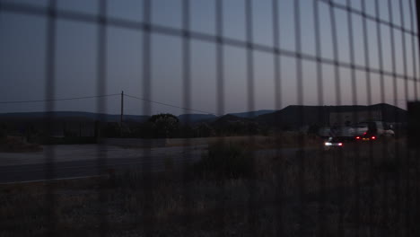 Mirando-La-Carretera-Rural-Al-Atardecer-A-Través-De-Una-Valla-Metálica-De-Alambre