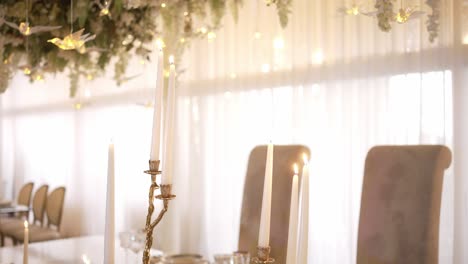 elegant table setup with tall candles and floral ceiling decor, softly lit by natural light