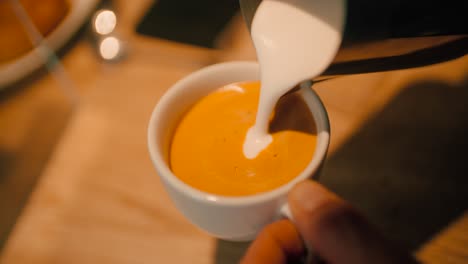 Close-up-hand-of-barista-pouring-latte-art-with-espresso-and-milk-froth-in-white-hot-ceramic-cup