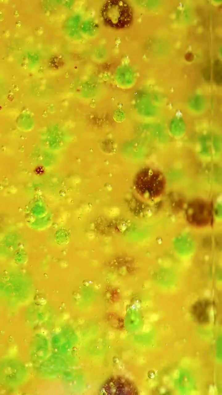 Reação química vibrante com gotas coloridas num béquer, exibindo movimento e separação dinâmicos sob iluminação brilhante.