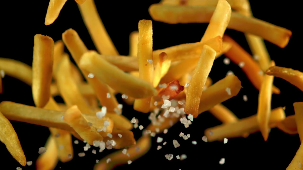 Golden French Fries Falling and Being Salted in Slow Motion