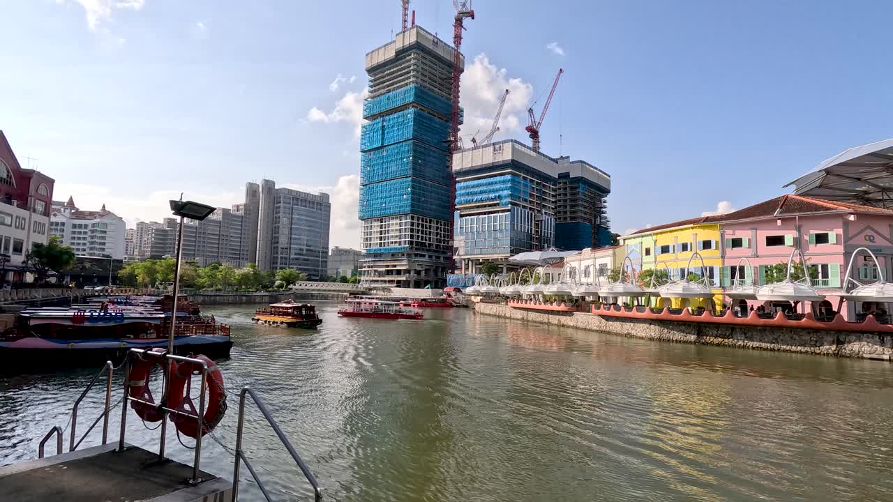 Tourist riverboat moves along Singapore River past Clarke Quay, modern buildings, and construction under daylight