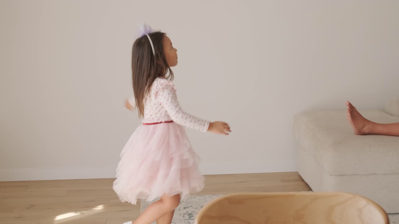 una joven baila alegremente en una sala de estar luminosa y acogedora. lleva un vestido rosado con un diseño de corazón, moviéndose juguetón en el espacio minimalista iluminado por el sol con decoración neutral y luz natural suave.