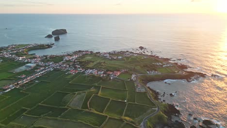 coastal village surrounded by green fields and rocky coastline at sunrise, aerial view