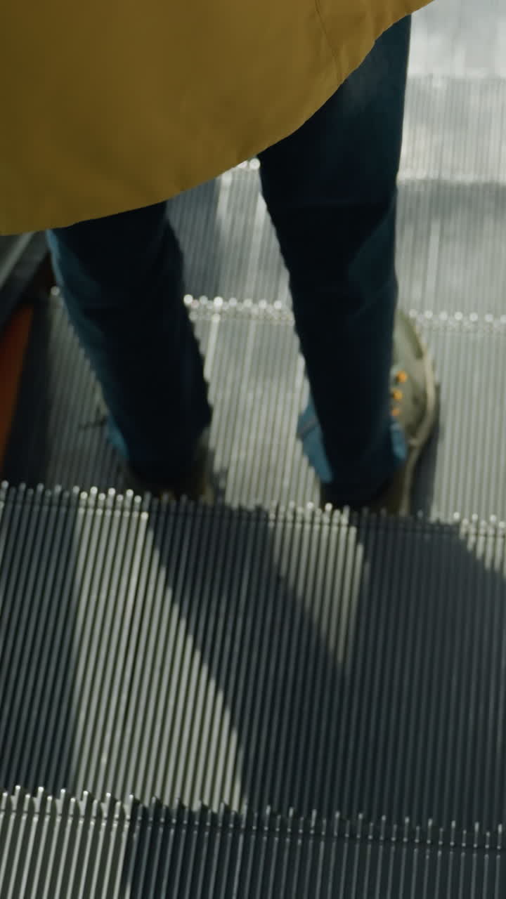 파란 청바지와 스니커를 입은 사람의 다리를 포착하는 클로즈업, 에스컬레이터를 내려가는 동안, 초점은 바쁜 쇼핑몰 설정에서 에스클레이터 계단의 움직임과 세부 사항에 있습니다.