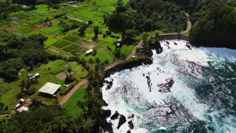 Una-Toma-De-Drones-De-La-Costa-De-Maui,-Hawai,-Mientras-Las-Olas-Chocan-Contra-La-Costa-De-Roca-Negra,-Con-Tierras-De-Cultivo-Y-Caminos-De-Tierra-Al-Fondo