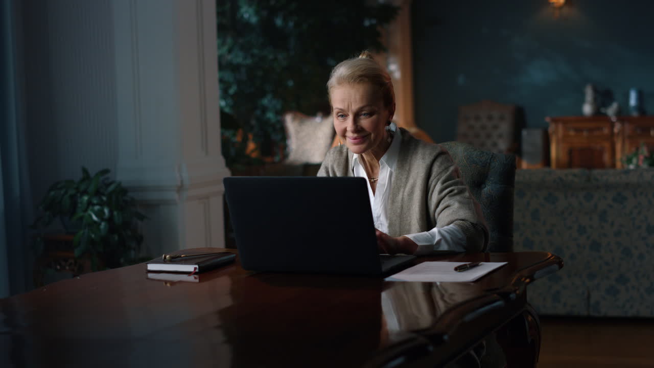 Smiling old woman reading good news on laptop computer at home
