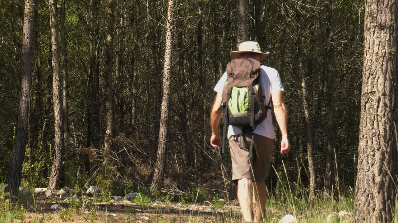 hombre con equipo de senderismo y mochila caminando por un sendero forestal
