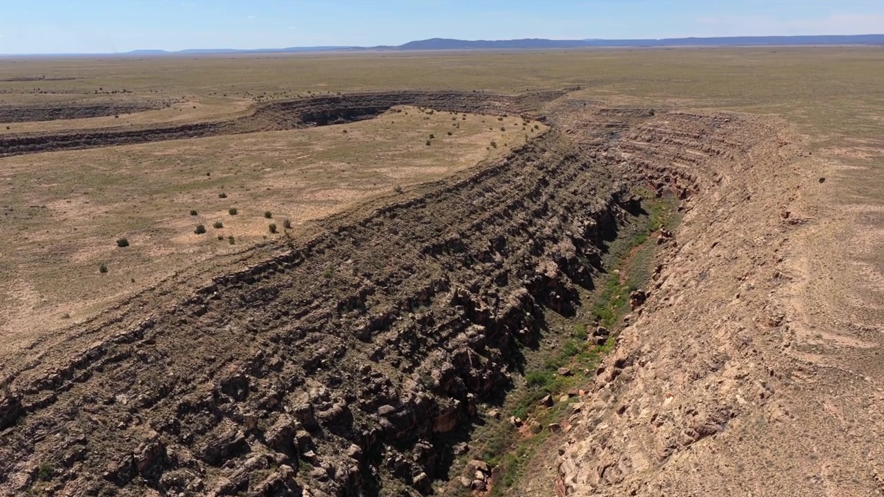 Volo di drone 4K UHD sopra una gola profonda e aspra scavata nel vasto deserto dell'Arizona. Le ripide scogliere rocciose di questo canyon fluviale secco offrono un paesaggio epico per il turismo d'avventura nella natura selvaggia.