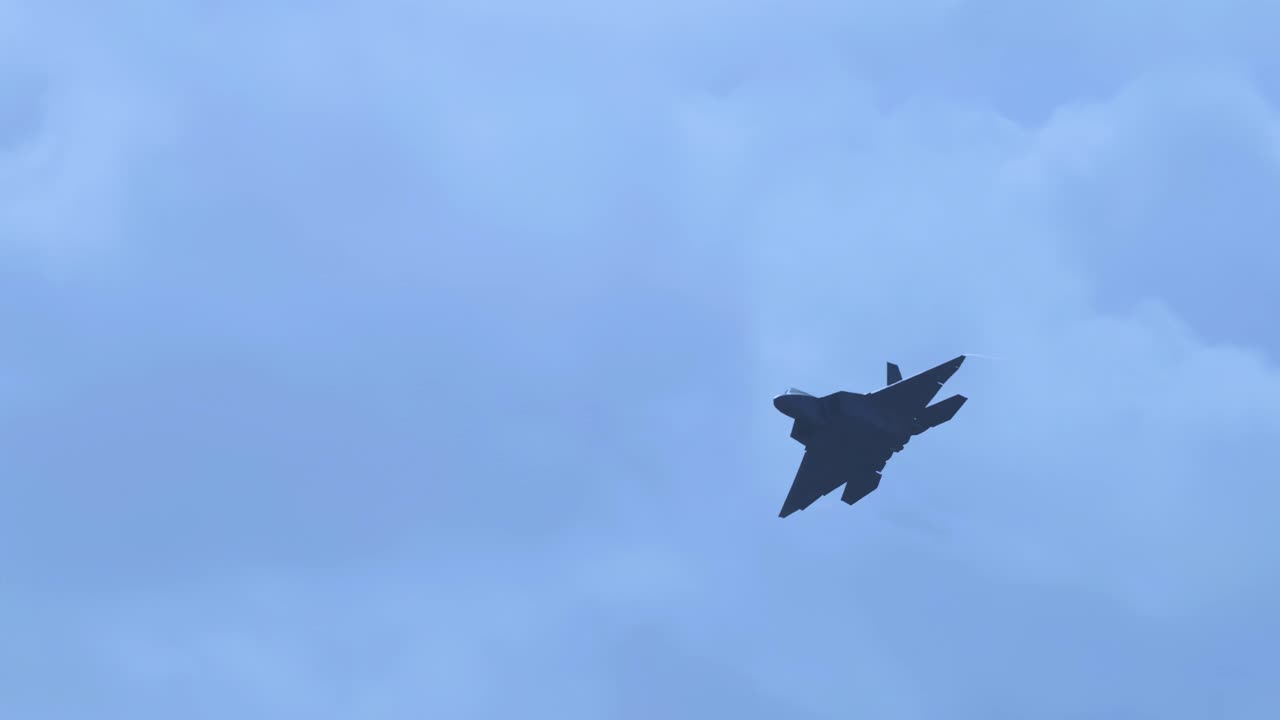 A jet fighter executes dynamic aerial maneuvers against a backdrop of cloudy skies, captured in smooth motion with steady camera work