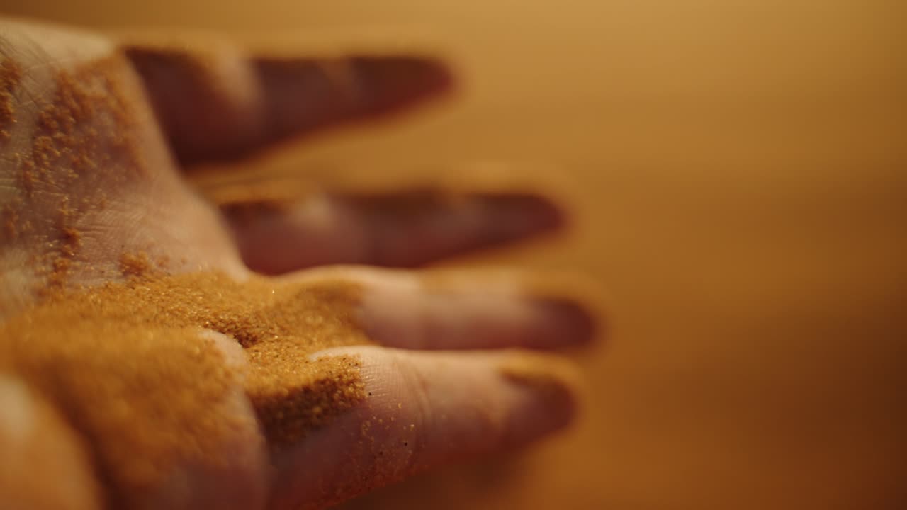 Close-up of a hand releasing fine Sahara sand, grains cascading in warm light, symbolizing time and the vastness of Morocco’s desert
