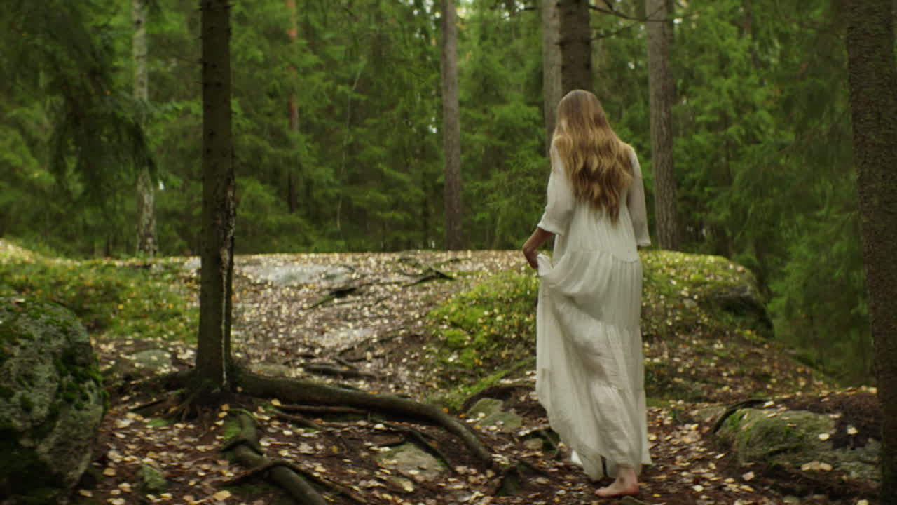Una donna con un lungo abito bianco cammina attraverso una foresta.