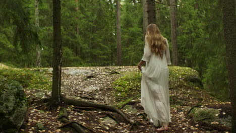 a woman in a long white dress walks through a forest