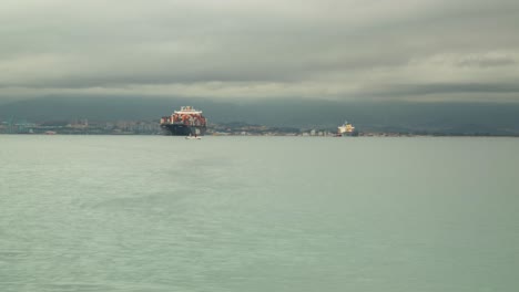 Buque-Portacontenedores-Amarrado-Cerca-Del-Puerto-De-Gibraltar,-Vista-De-Lapso-De-Tiempo-Con-Nubes-Tormentosas