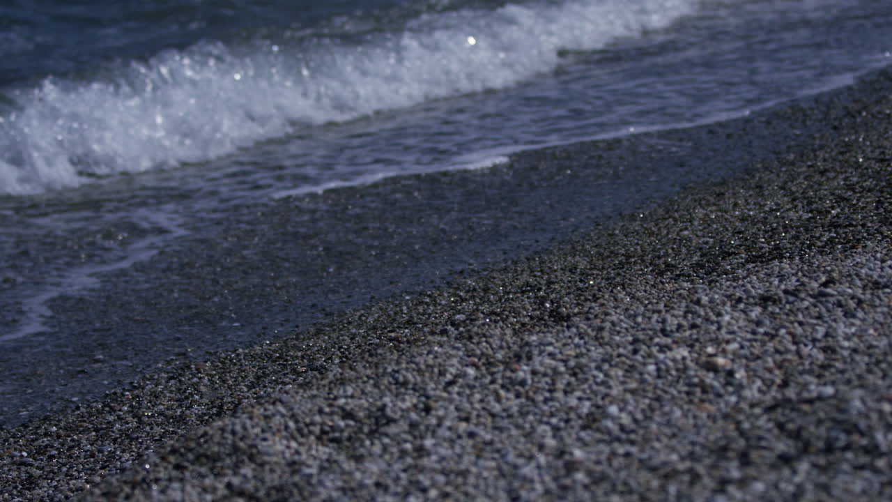 Small waves roll in to the shore at the water's edge on a pebble beach