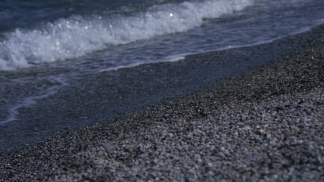 small waves roll in to the shore at the water's edge on a pebble beach