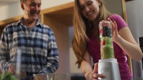 padre caucásico mayor sonriente e hija adolescente preparando una bebida saludable en la cocina
