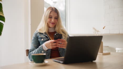 woman using phone and laptop in a cafe