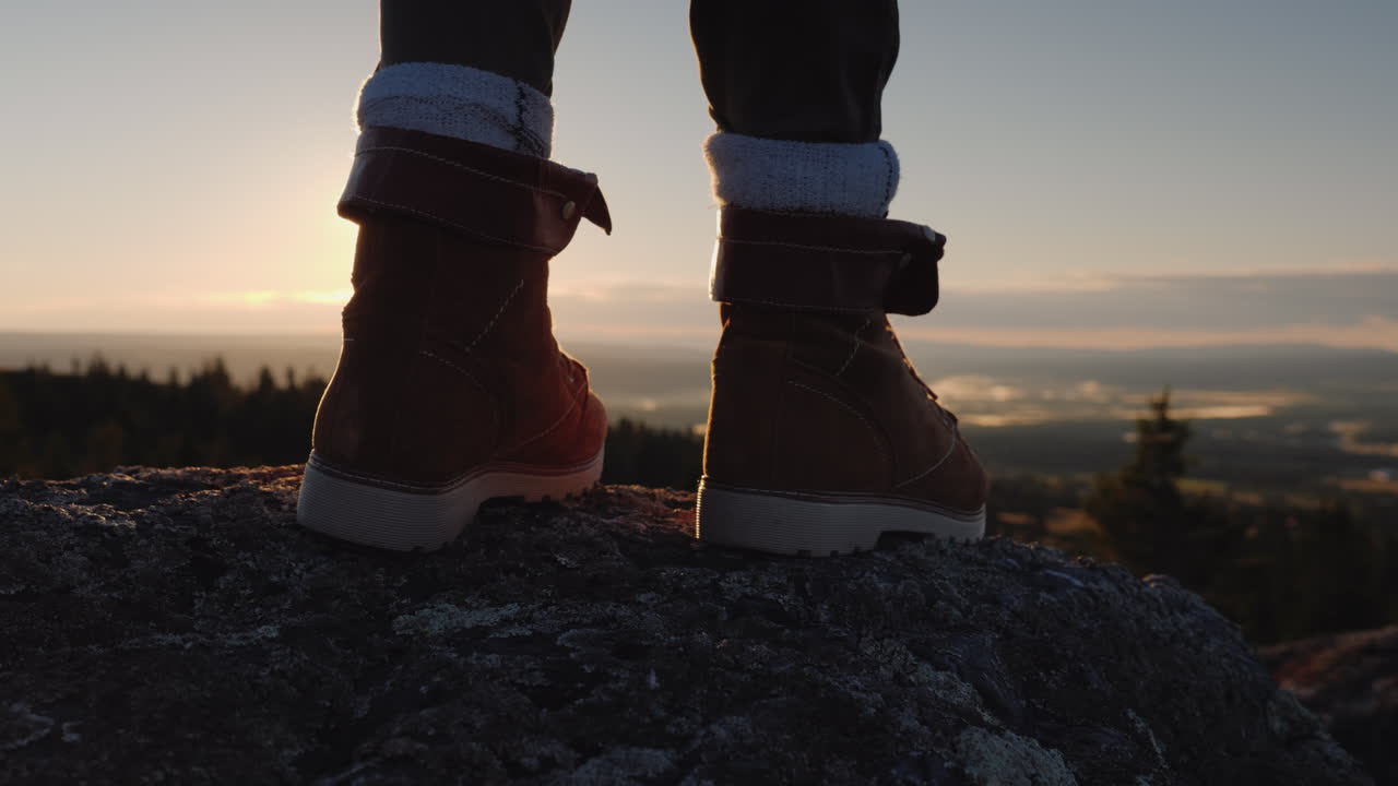 los pies del viajero en la cima del pico a través de ellos brilla el sol naciente y el hermoso paisaje