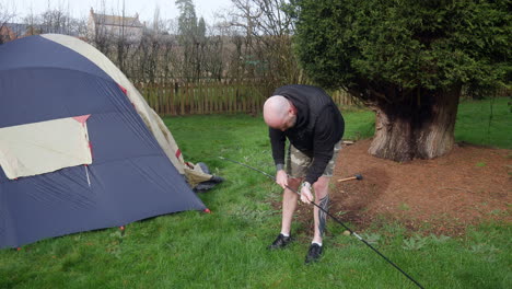 a man in a field campsite putting tent poles together next to a tent whilst camping in a field in the countryside