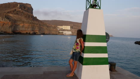 young woman rests on a sea lamp watching bay and coast cliff in canary islands