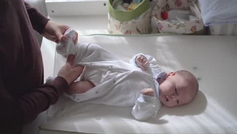 Crop-dad-dressing-cute-baby-on-table-in-house